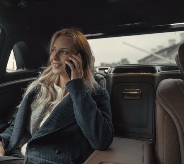 A smiling woman on a phone call in the back seat of a car after a meeting