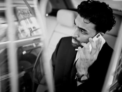 A man in a suit in the back of a car listens on the phone with a worried look