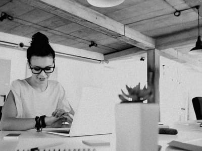 A woman checks her watch while working at a laptop before a meeting