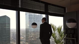 An executive in a suit stands at a high-rise office window