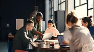 An agency team gathers around a laptop while one person explains